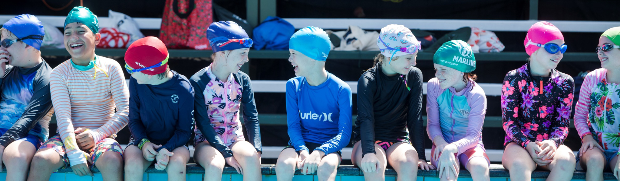 Students in togs sitting on side of swimming pool