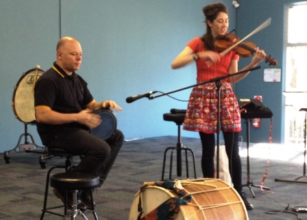 Man playing bongo drum and lady playing violin